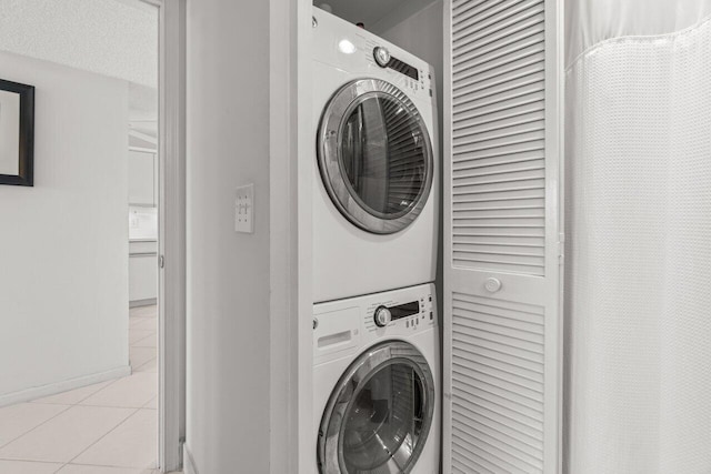 laundry room featuring stacked washer and dryer, a textured ceiling, and light tile patterned floors