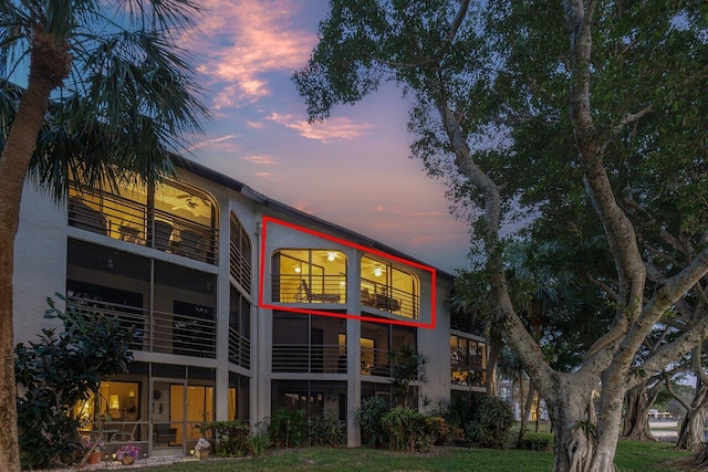 back house at dusk featuring a balcony and a lawn