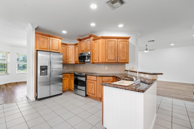 kitchen featuring sink, light tile patterned floors, dark stone countertops, stainless steel appliances, and kitchen peninsula