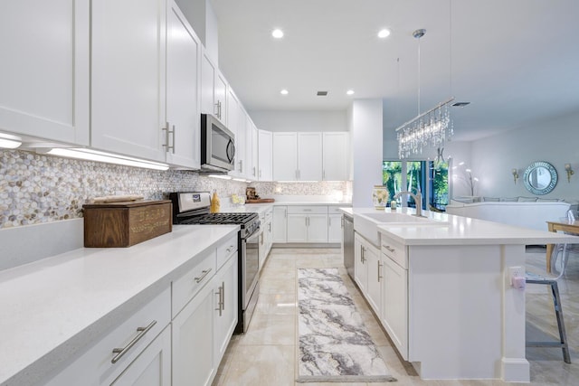 kitchen featuring a kitchen island with sink, hanging light fixtures, stainless steel appliances, a kitchen breakfast bar, and white cabinets