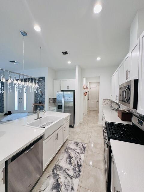 kitchen with stainless steel appliances, white cabinetry, hanging light fixtures, and sink