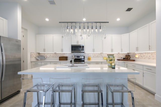 kitchen with white cabinetry, a breakfast bar area, stainless steel appliances, and a center island with sink