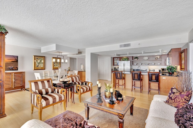 living room with a chandelier, light hardwood / wood-style flooring, and a textured ceiling