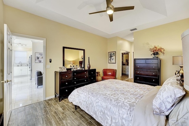 bedroom with sink, connected bathroom, light hardwood / wood-style floors, a raised ceiling, and a closet