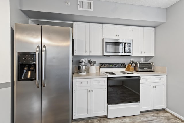 kitchen with appliances with stainless steel finishes, light hardwood / wood-style floors, a textured ceiling, and white cabinets