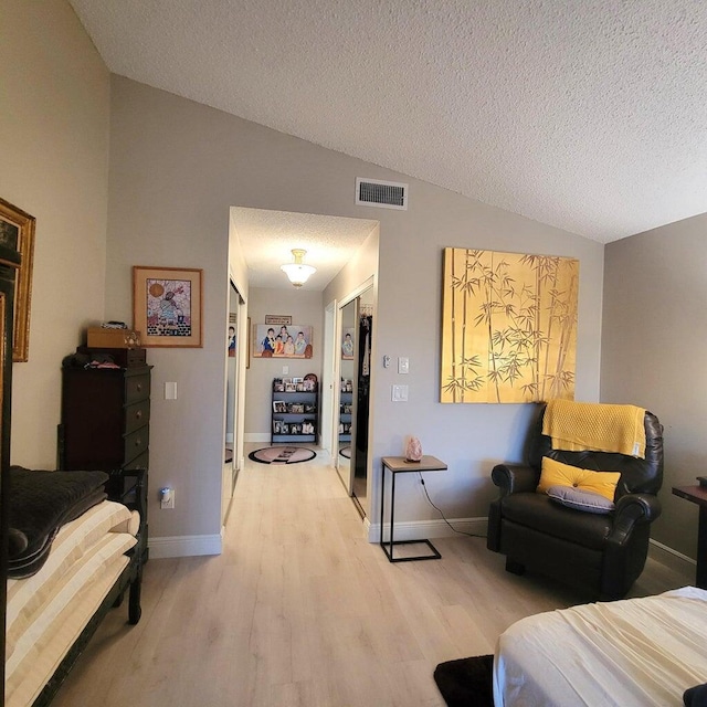 bedroom featuring lofted ceiling, a textured ceiling, and light wood-type flooring