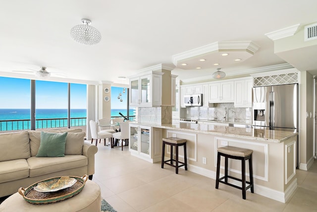 kitchen featuring white cabinetry, a kitchen breakfast bar, light stone counters, stainless steel refrigerator with ice dispenser, and a water view