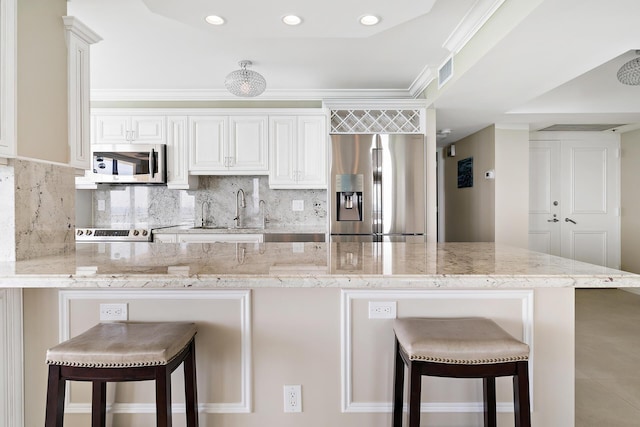 kitchen featuring sink, stainless steel appliances, a kitchen breakfast bar, light stone countertops, and white cabinets