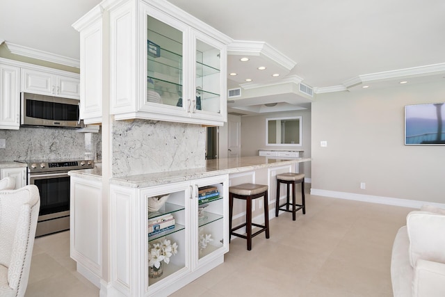 kitchen featuring appliances with stainless steel finishes, white cabinets, light stone counters, and decorative backsplash