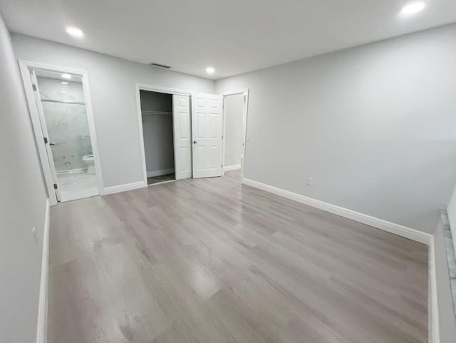 unfurnished bedroom featuring ensuite bath, light hardwood / wood-style floors, and a closet