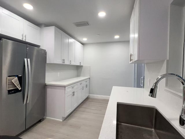 kitchen with sink, stainless steel fridge, white cabinets, and light wood-type flooring