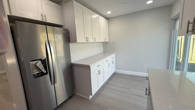 kitchen with stainless steel refrigerator with ice dispenser, tasteful backsplash, light stone counters, light wood-type flooring, and white cabinets