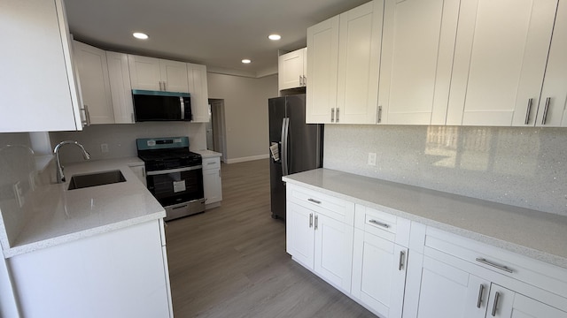 kitchen with appliances with stainless steel finishes, tasteful backsplash, white cabinetry, sink, and light hardwood / wood-style floors