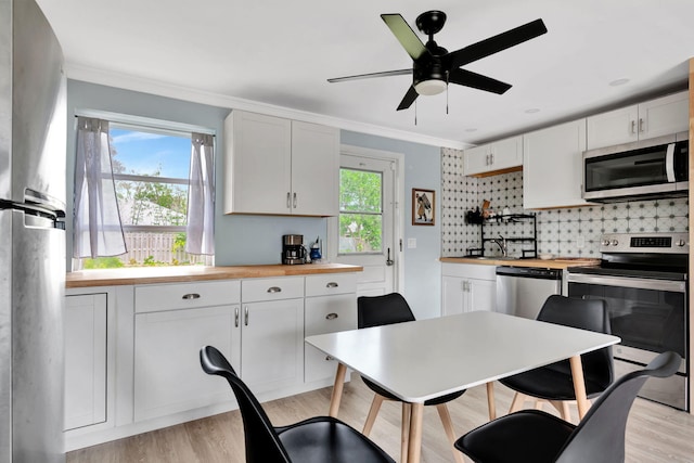 kitchen featuring appliances with stainless steel finishes, white cabinetry, crown molding, butcher block countertops, and decorative backsplash