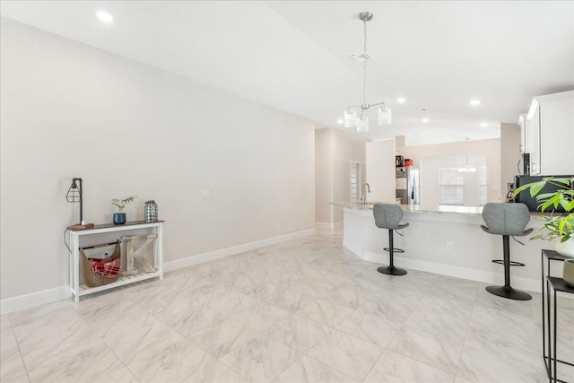 kitchen featuring a breakfast bar, light stone counters, kitchen peninsula, a notable chandelier, and white cabinets