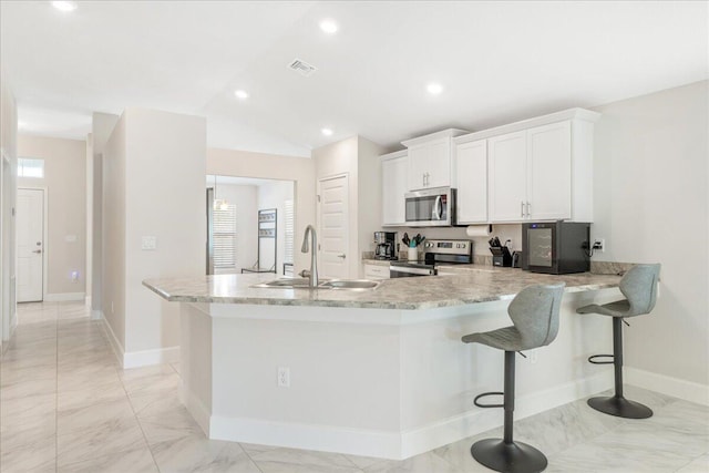 kitchen with appliances with stainless steel finishes, a breakfast bar, sink, white cabinets, and kitchen peninsula