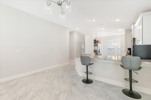 kitchen featuring a kitchen bar, sink, light stone counters, stainless steel appliances, and white cabinets