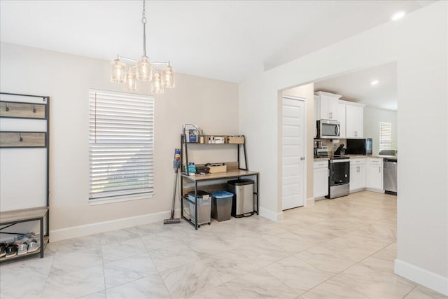 interior space with appliances with stainless steel finishes, lofted ceiling, white cabinets, hanging light fixtures, and an inviting chandelier