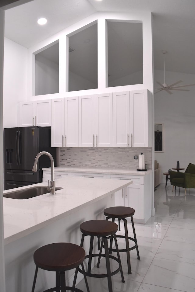 kitchen featuring a breakfast bar, sink, black fridge with ice dispenser, and white cabinets