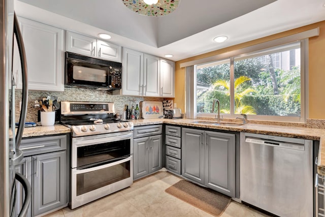 kitchen with appliances with stainless steel finishes, sink, gray cabinetry, backsplash, and light stone counters