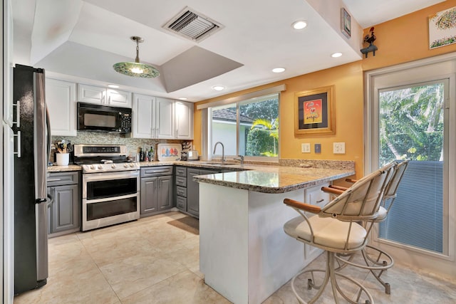 kitchen with pendant lighting, gray cabinets, stainless steel appliances, stone countertops, and kitchen peninsula