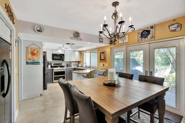 dining area with sink, an inviting chandelier, a textured ceiling, and french doors