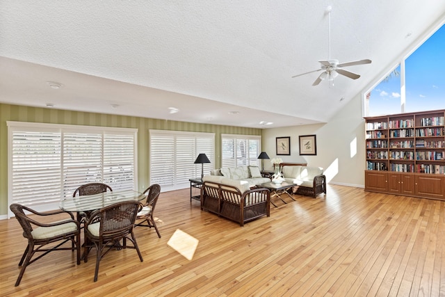 living room featuring ceiling fan, light hardwood / wood-style flooring, high vaulted ceiling, and a textured ceiling