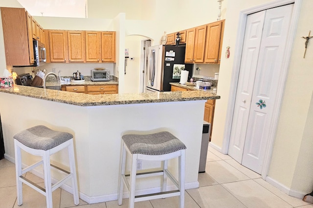 kitchen with stainless steel appliances, light tile patterned flooring, light stone countertops, and a kitchen breakfast bar