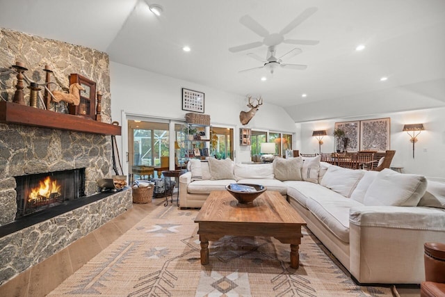 living room featuring ceiling fan, a stone fireplace, vaulted ceiling, and light wood-type flooring