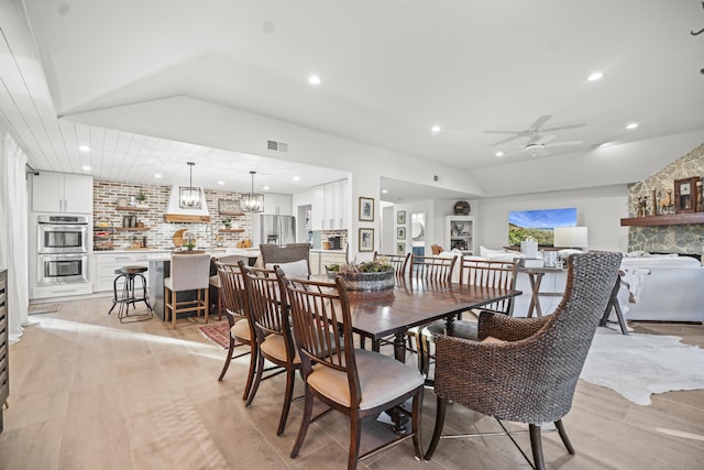 dining room with ceiling fan with notable chandelier, vaulted ceiling, and light wood-type flooring