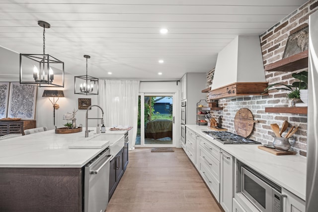 kitchen with appliances with stainless steel finishes, white cabinetry, hanging light fixtures, light stone counters, and custom range hood