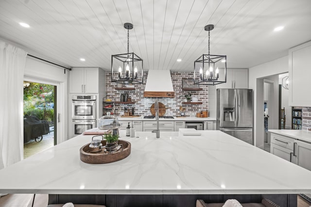 kitchen featuring a large island with sink, light stone countertops, appliances with stainless steel finishes, and hanging light fixtures