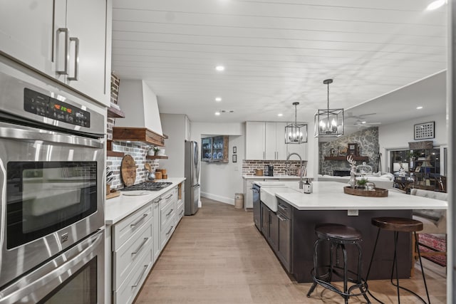 kitchen featuring decorative light fixtures, a kitchen breakfast bar, an island with sink, white cabinets, and backsplash