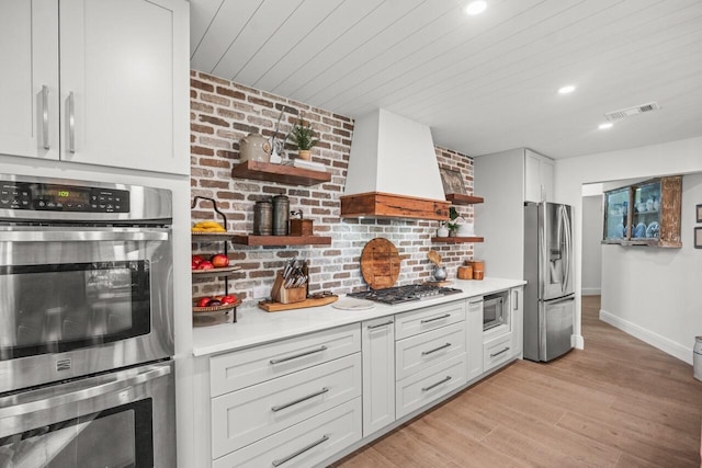 kitchen with white cabinetry, light hardwood / wood-style flooring, premium range hood, and appliances with stainless steel finishes