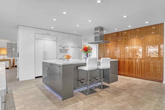 kitchen featuring a kitchen bar, paneled built in refrigerator, island exhaust hood, a large island, and white cabinets