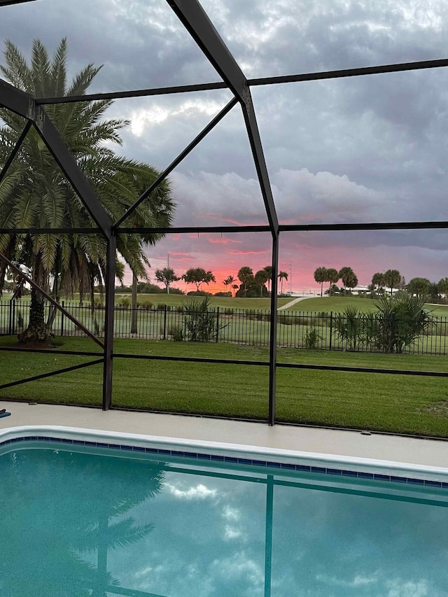 pool at dusk featuring a lanai and a yard