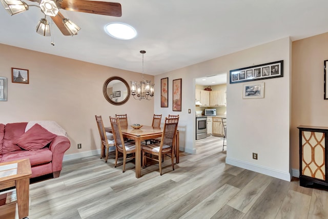 dining space with ceiling fan with notable chandelier and light hardwood / wood-style flooring