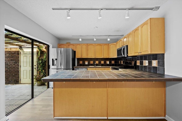 kitchen featuring stainless steel appliances, tile counters, decorative backsplash, and kitchen peninsula