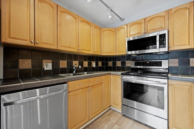 kitchen with light wood-type flooring, sink, tile countertops, and appliances with stainless steel finishes