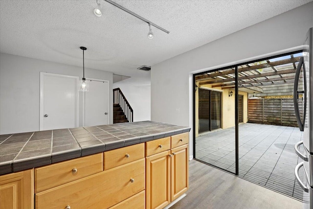 kitchen with light wood-type flooring, tile countertops, a textured ceiling, and stainless steel refrigerator