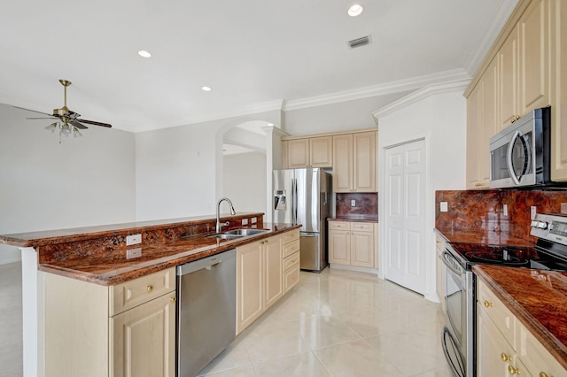 kitchen with cream cabinetry, a sink, arched walkways, a ceiling fan, and appliances with stainless steel finishes