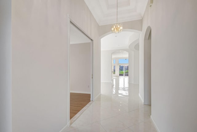 hall with an inviting chandelier, a tray ceiling, and ornamental molding