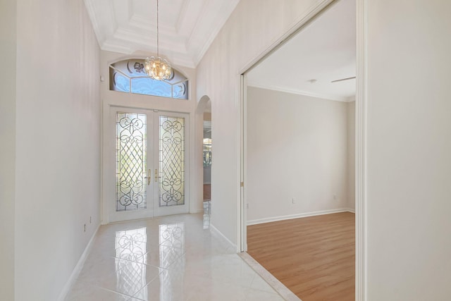 tiled foyer featuring french doors, a towering ceiling, ornamental molding, and a chandelier