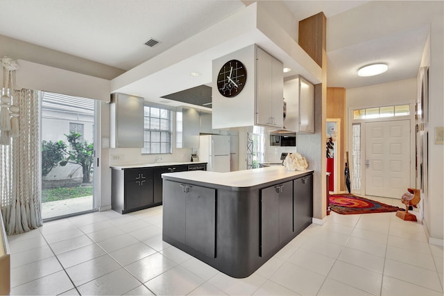 kitchen featuring white fridge, sink, light tile patterned floors, and kitchen peninsula