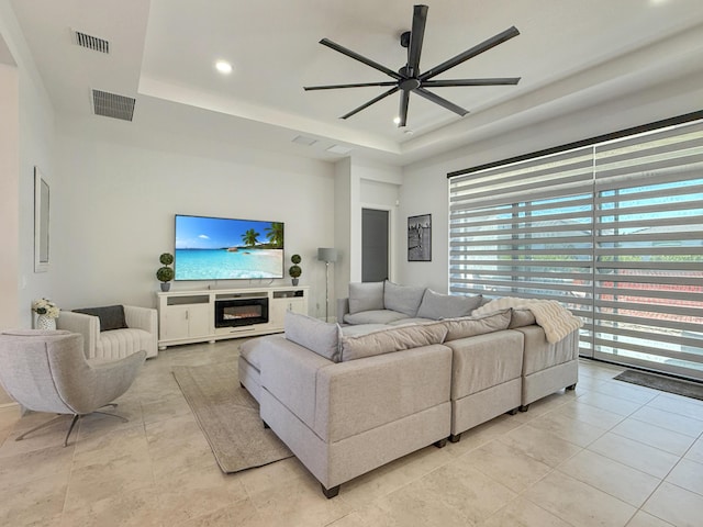 tiled living room with a raised ceiling and ceiling fan