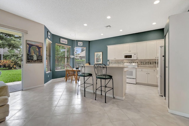 kitchen featuring a kitchen bar, white cabinetry, tasteful backsplash, a center island, and white appliances