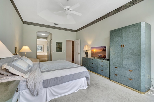 carpeted bedroom featuring a raised ceiling, crown molding, connected bathroom, and ceiling fan