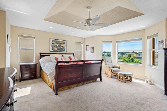 bedroom with ceiling fan, a raised ceiling, light carpet, and a textured ceiling