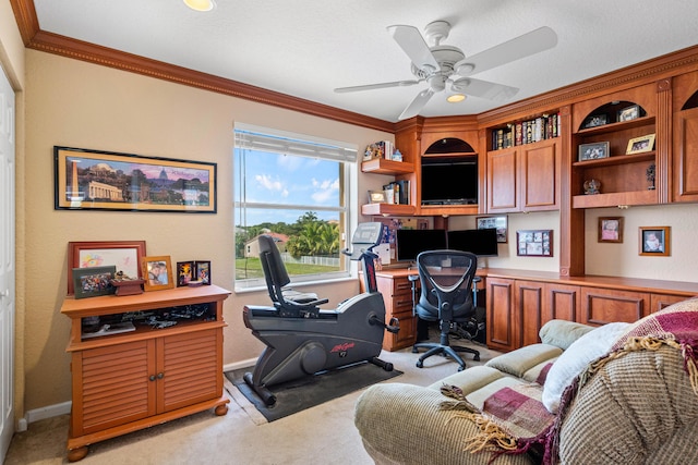 carpeted office with built in desk, ornamental molding, and ceiling fan