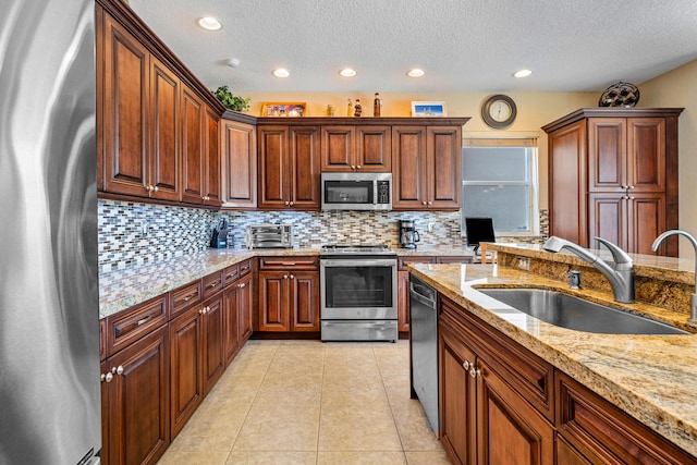 kitchen featuring sink, light tile patterned floors, stainless steel appliances, light stone countertops, and backsplash